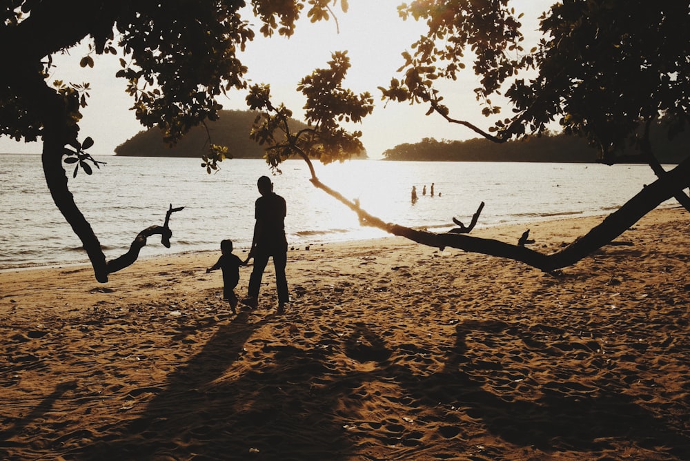 2 person standing on beach shore during sunset