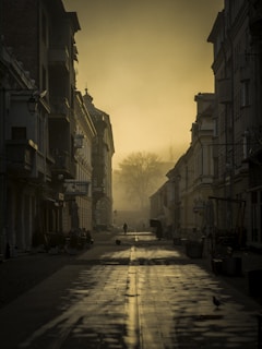 A misty old street in Santiago de Compostela at dawn, with ancient stone buildings and a shadowy figure walking.
