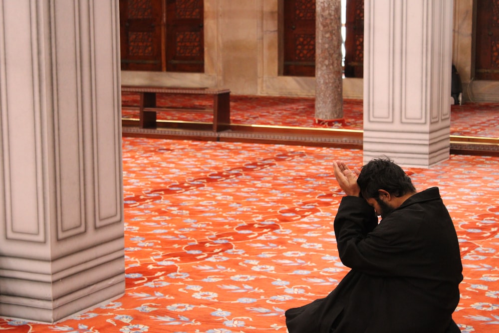 man in black robe sitting on red floor