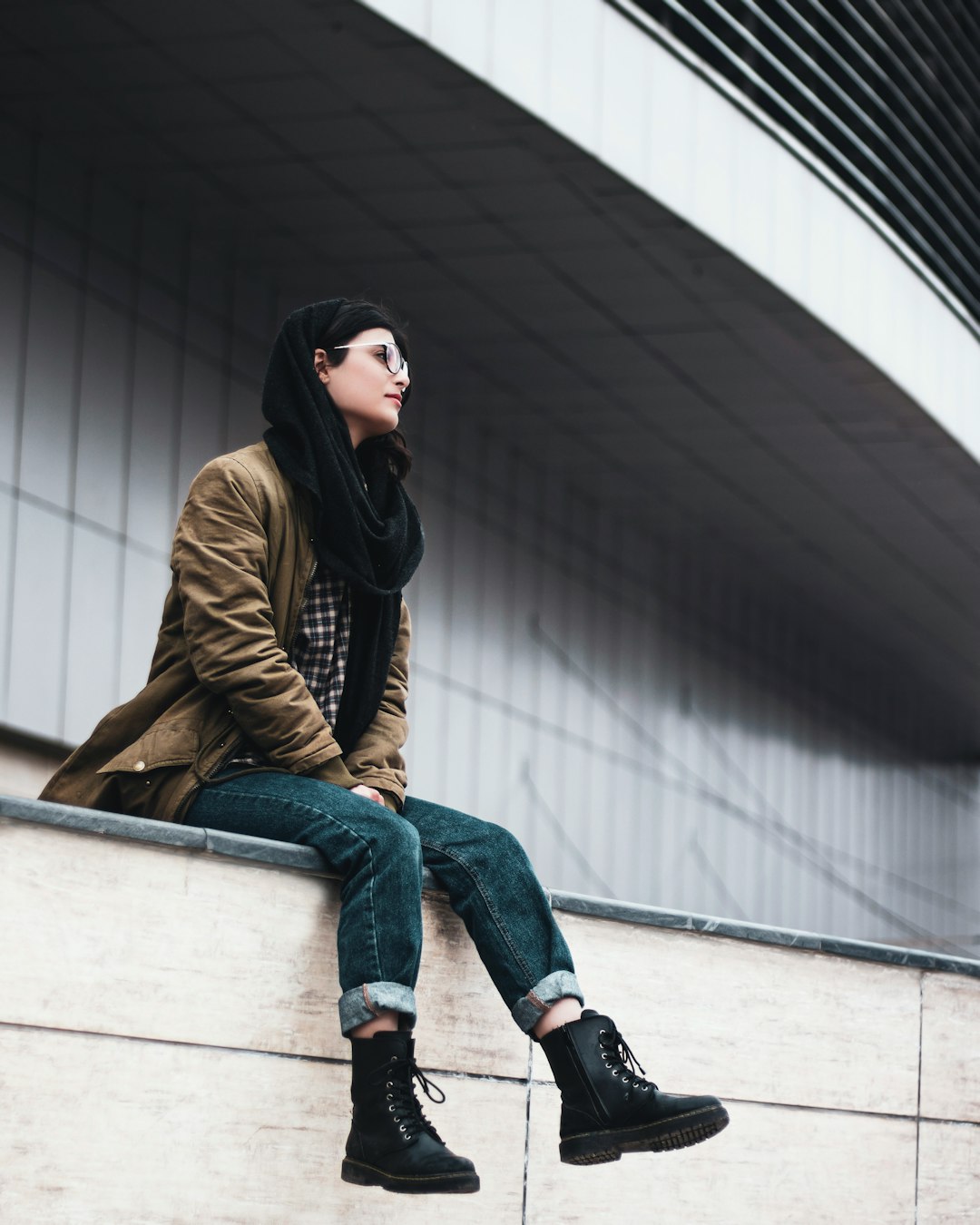 woman in brown jacket and blue denim jeans sitting on white concrete bench