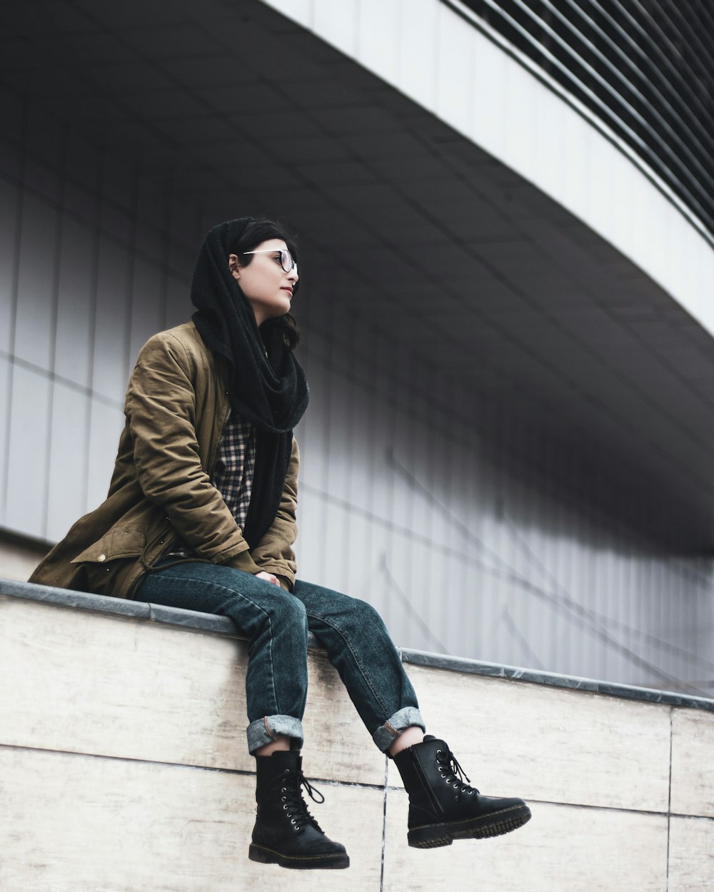 woman in brown jacket and blue denim jeans sitting on white concrete bench