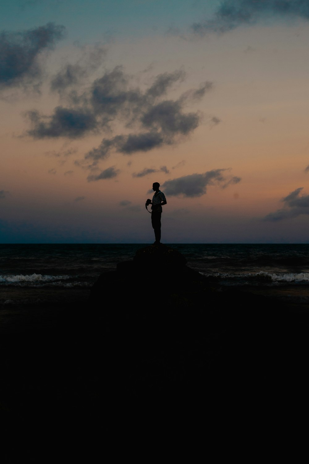 silhouette of man standing on rock formation near sea during sunset