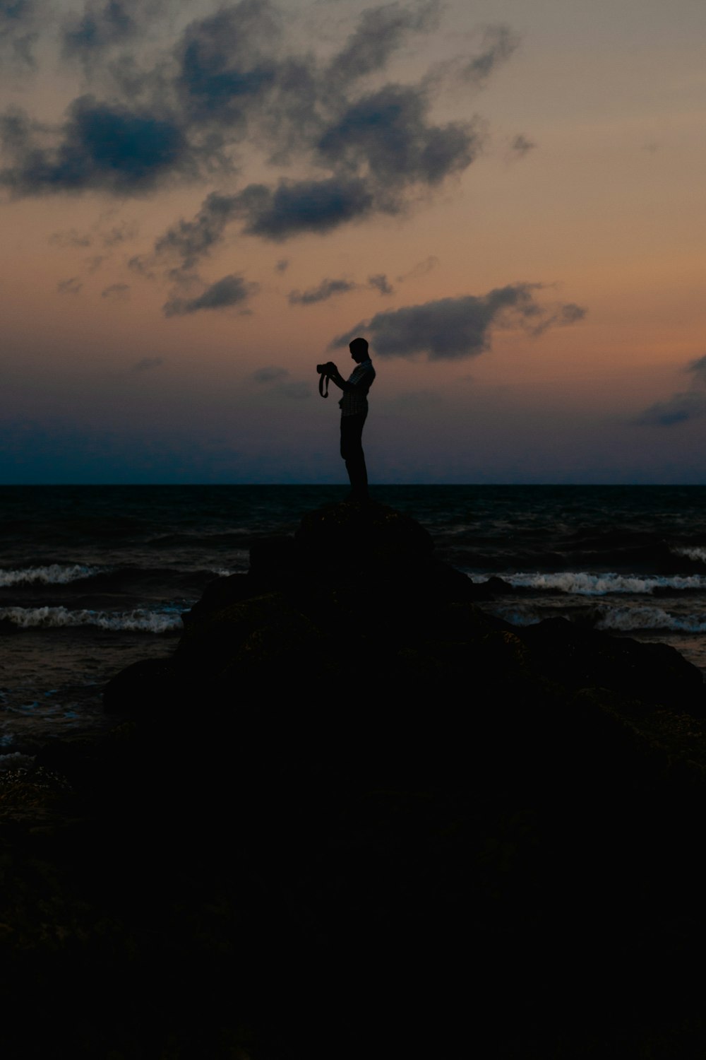 silhouette of man standing on rock formation near sea during sunset