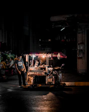 A masked volunteer handing a meal to a grateful person under a streetlamp’s glow with subtle smoke in the background.