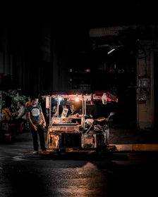 A masked volunteer handing a meal to a grateful person under a streetlamp’s glow with subtle smoke in the background.