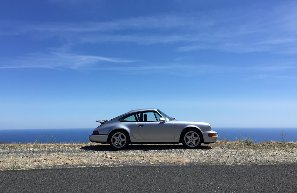 Weißes Mercedes Benz Coupé tagsüber auf grauem Sand unter blauem Himmel