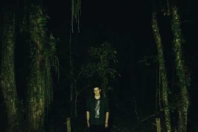 A rugged survivor searching through a dense forest for supplies at dusk.