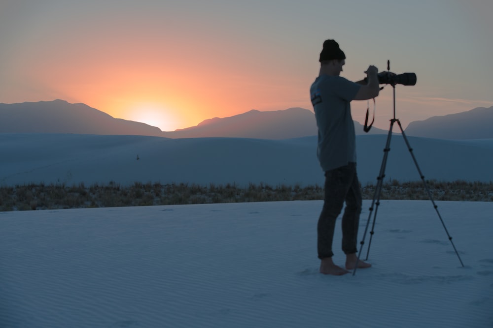 man in white shirt and black pants standing on snow covered ground during sunset