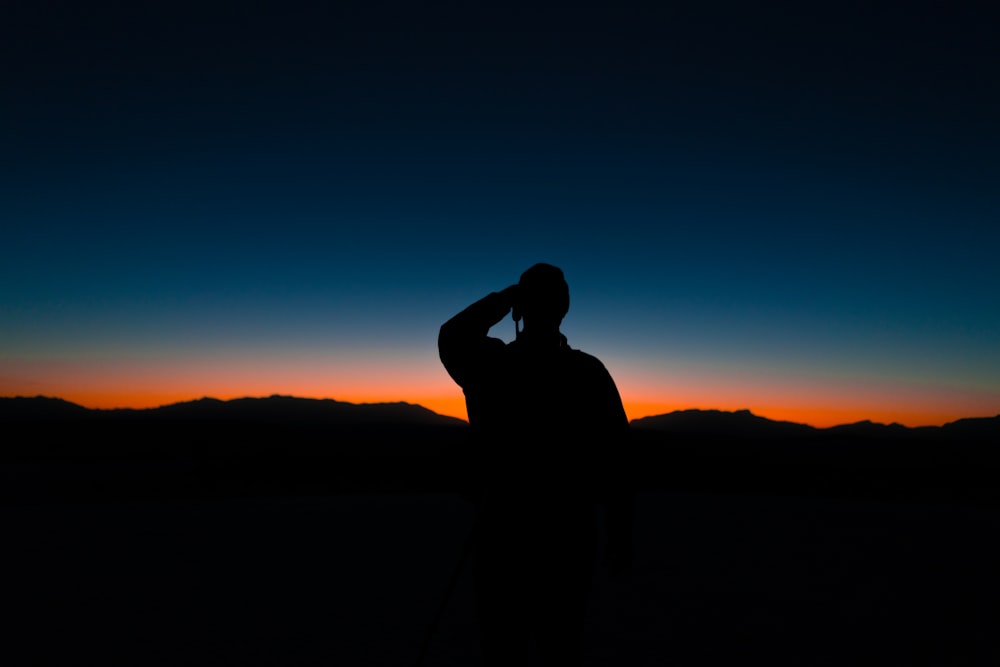 silhouette of man standing on hill during sunset