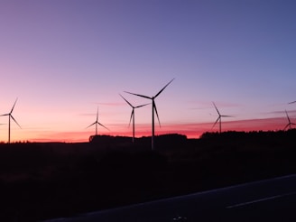 A panoramic view of a wind farm at sunset with turbines silhouetted against the colorful sky.