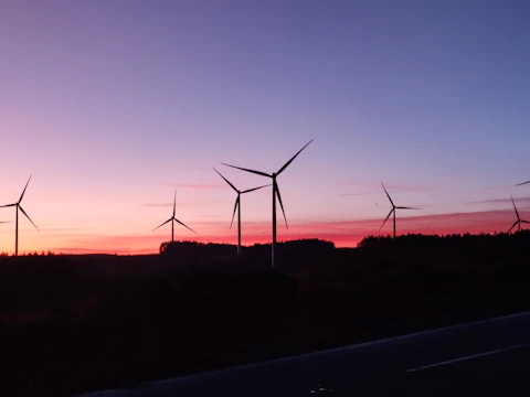 A wind farm at sunset with turbines silhouetted against a colorful sky.