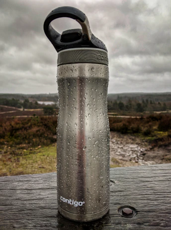 A sleek, insulated water bottle sitting on a rocky ledge with a mountain view.