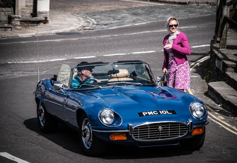 woman in pink long sleeve shirt standing beside blue bmw coupe