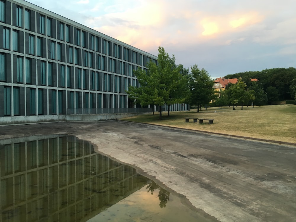 Graues Betongebäude in der Nähe grüner Bäume unter weißen Wolken tagsüber