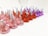 A group of chocolate candies wrapped in colorful foil are arranged in rows. The wrappers are in shades of pink, red, and purple, with each candy having a small paper tag protruding from the top.