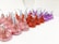 A group of chocolate candies wrapped in colorful foil are arranged in rows. The wrappers are in shades of pink, red, and purple, with each candy having a small paper tag protruding from the top.