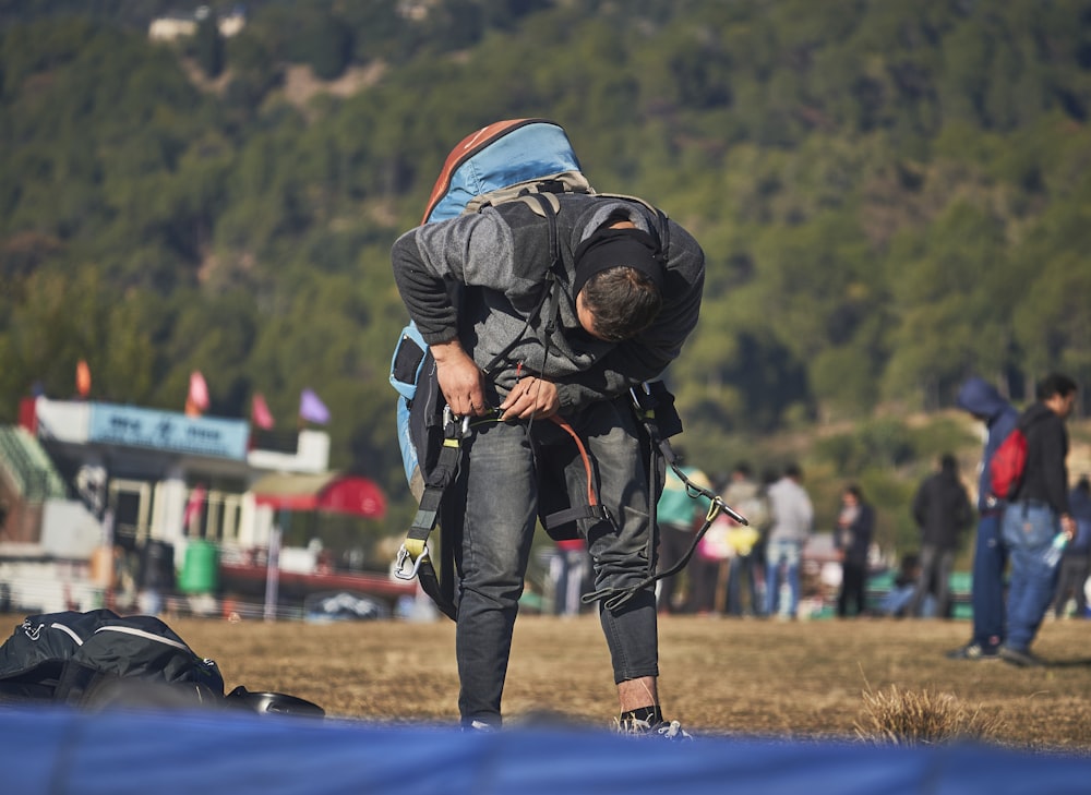 uomo in giacca nera e jeans blu in denim con zaino nero che cammina sul campo di erba verde