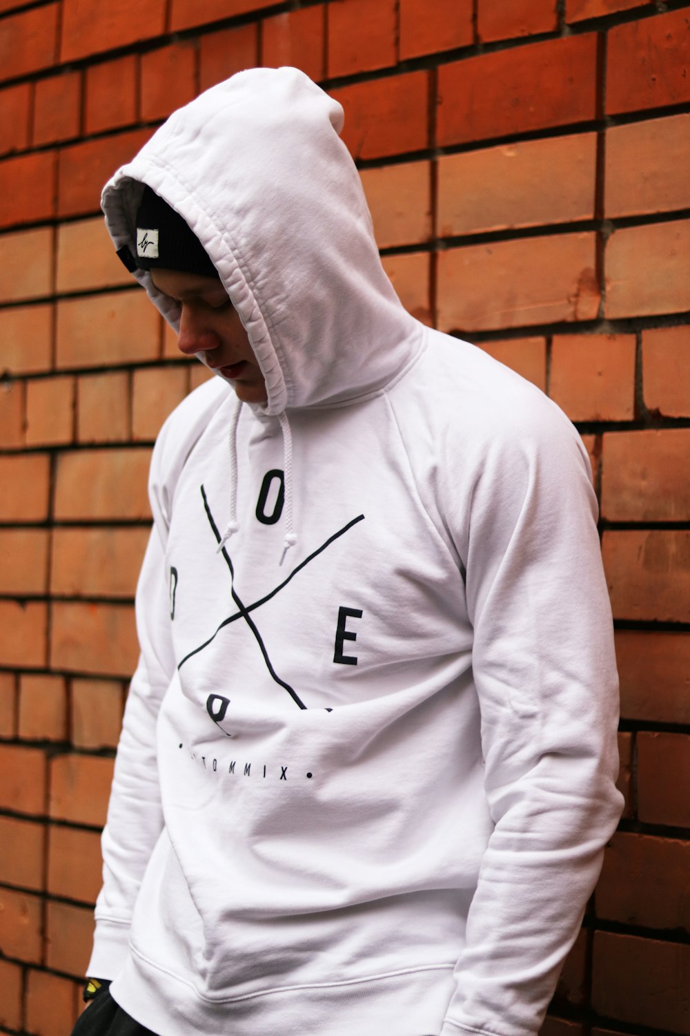 man in white nike hoodie standing beside brown brick wall