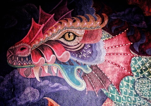 A vibrant, detailed painting of a dragon's head featuring intricate scales, sharp teeth, and a fierce eye. The dragon's colors are a mix of reds, purples, and greens, with a textured and stylized pattern throughout. The background includes swirling clouds, adding a dynamic and mystical atmosphere to the artwork.