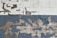 A brick wall with peeling paint, revealing layers of white, gray, and dark blue colors. The surface shows a mix of rough textures and exposed bricks, with old and worn paint giving it a weathered look.