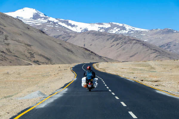 A motorcyclist on an empty road through bare high-altitude desert mountains