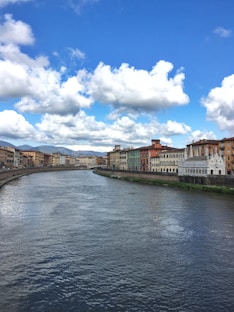 brown and white concrete building beside river under blue and white cloudy sky during daytime