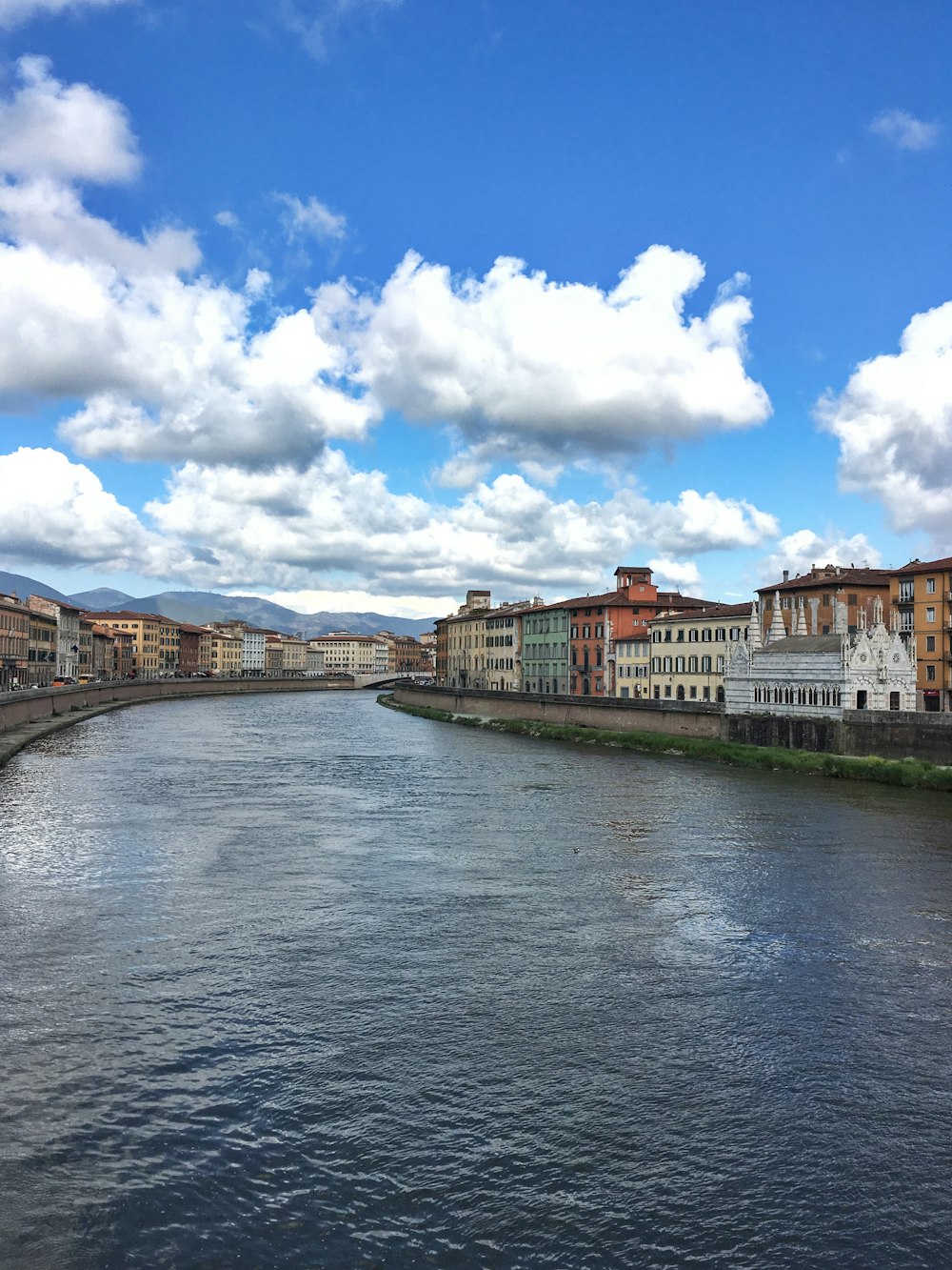 brown and white concrete building beside river under blue and white cloudy sky during daytime