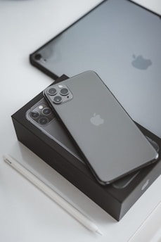 A smartphone with a triple-camera design is placed on its box, both exhibiting a sleek, modern look. Adjacent to it is a tablet with a similar color scheme along with a stylus placed nearby.