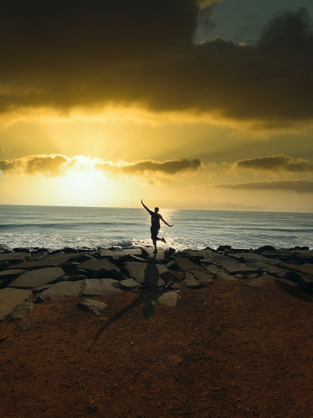 person jumping on rocky shore during sunset