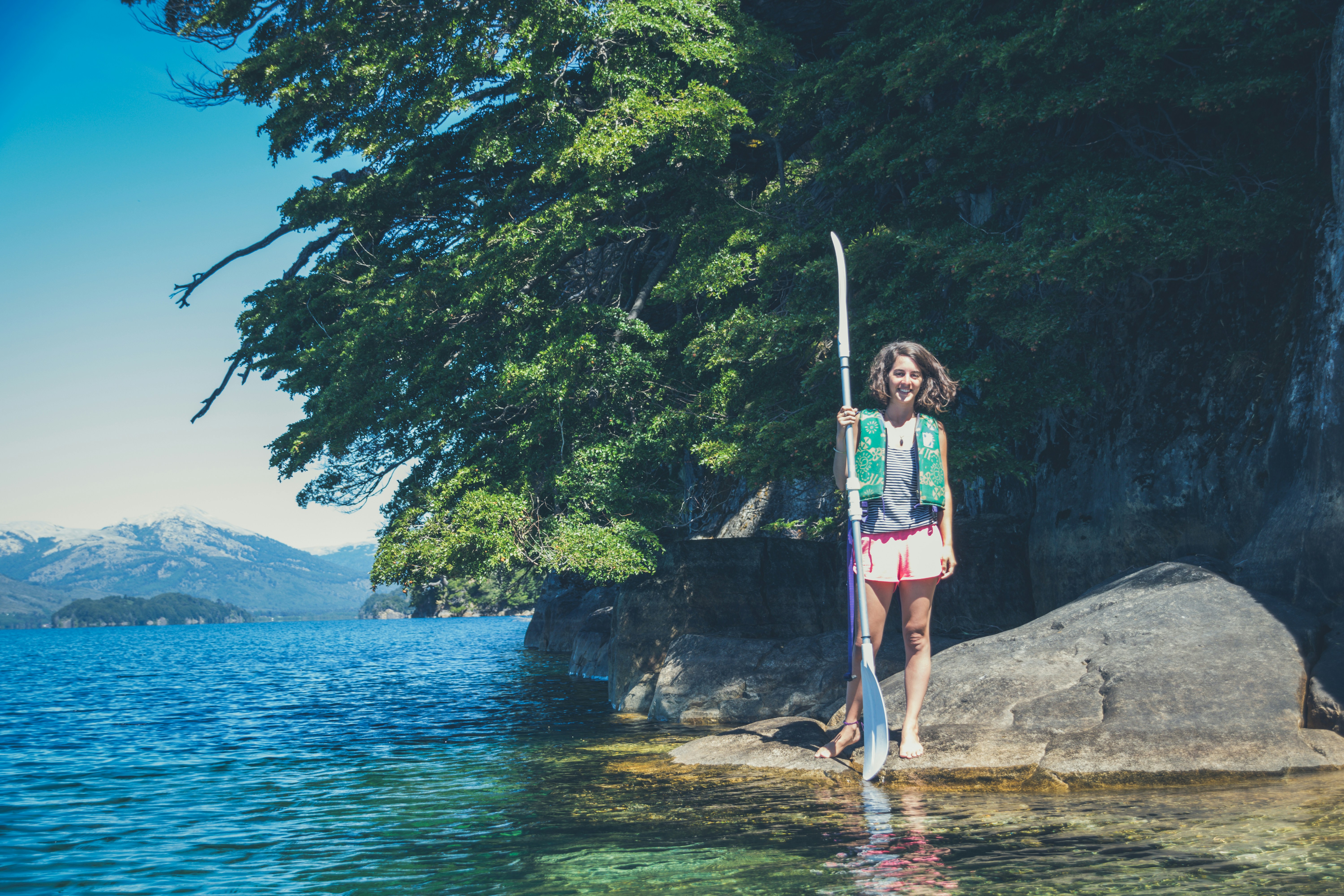woman in pink and white tank top standing on rock near body of water during daytime