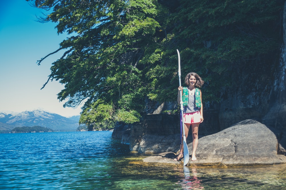 woman in pink and white tank top standing on rock near body of water during daytime