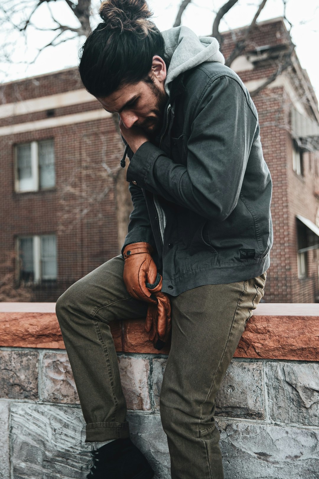 man in gray hoodie and brown pants sitting on brown concrete wall during daytime