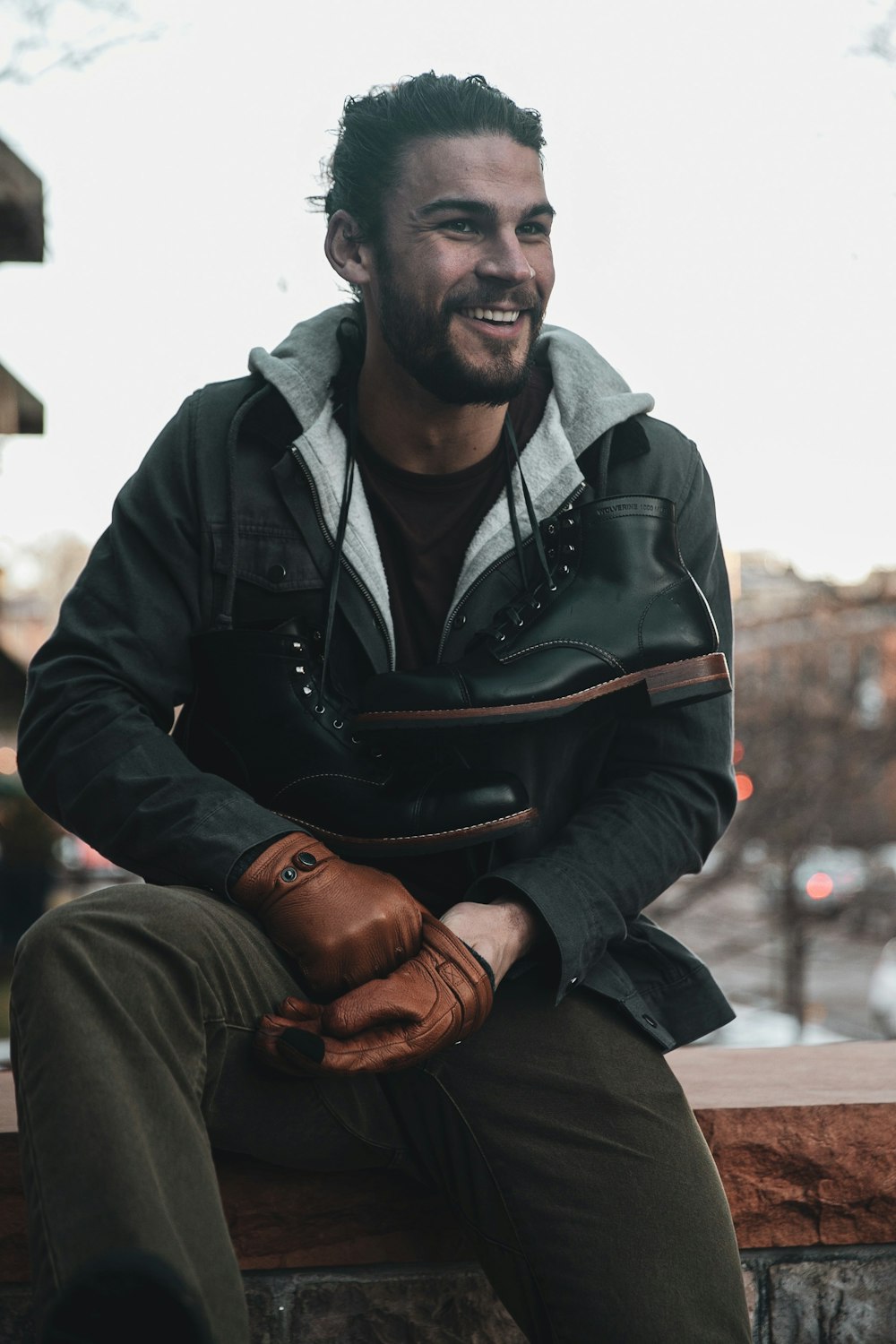 man in black leather jacket and brown pants sitting on brown wooden bench during daytime