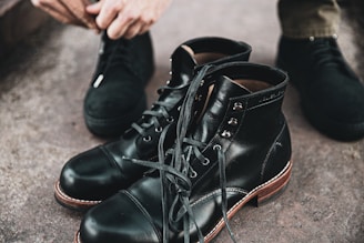 person holding black leather lace up boots
