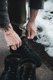 Hands applying waterproof wax to leather boots outdoors.