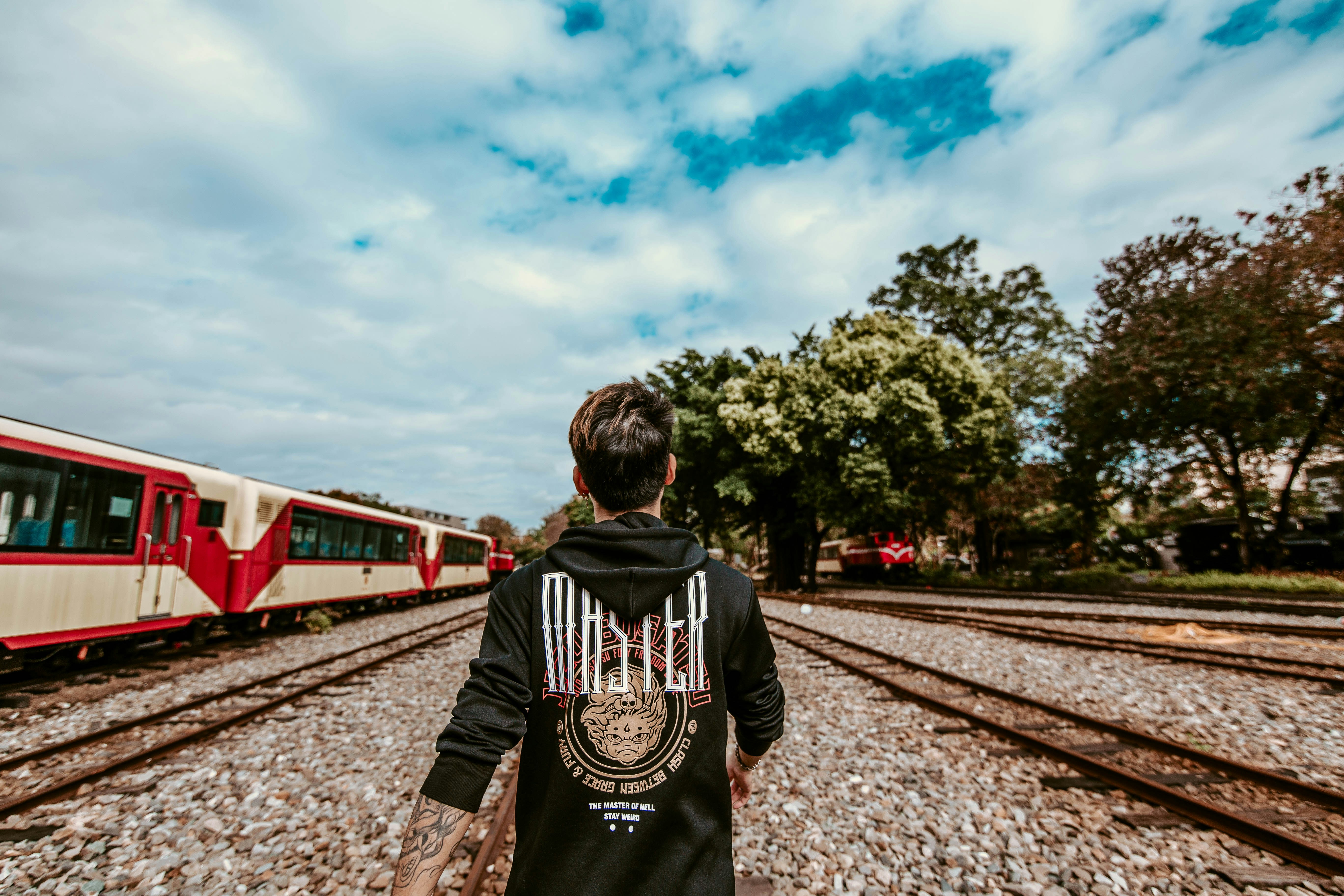 man in black and white hoodie standing on train rail during daytime