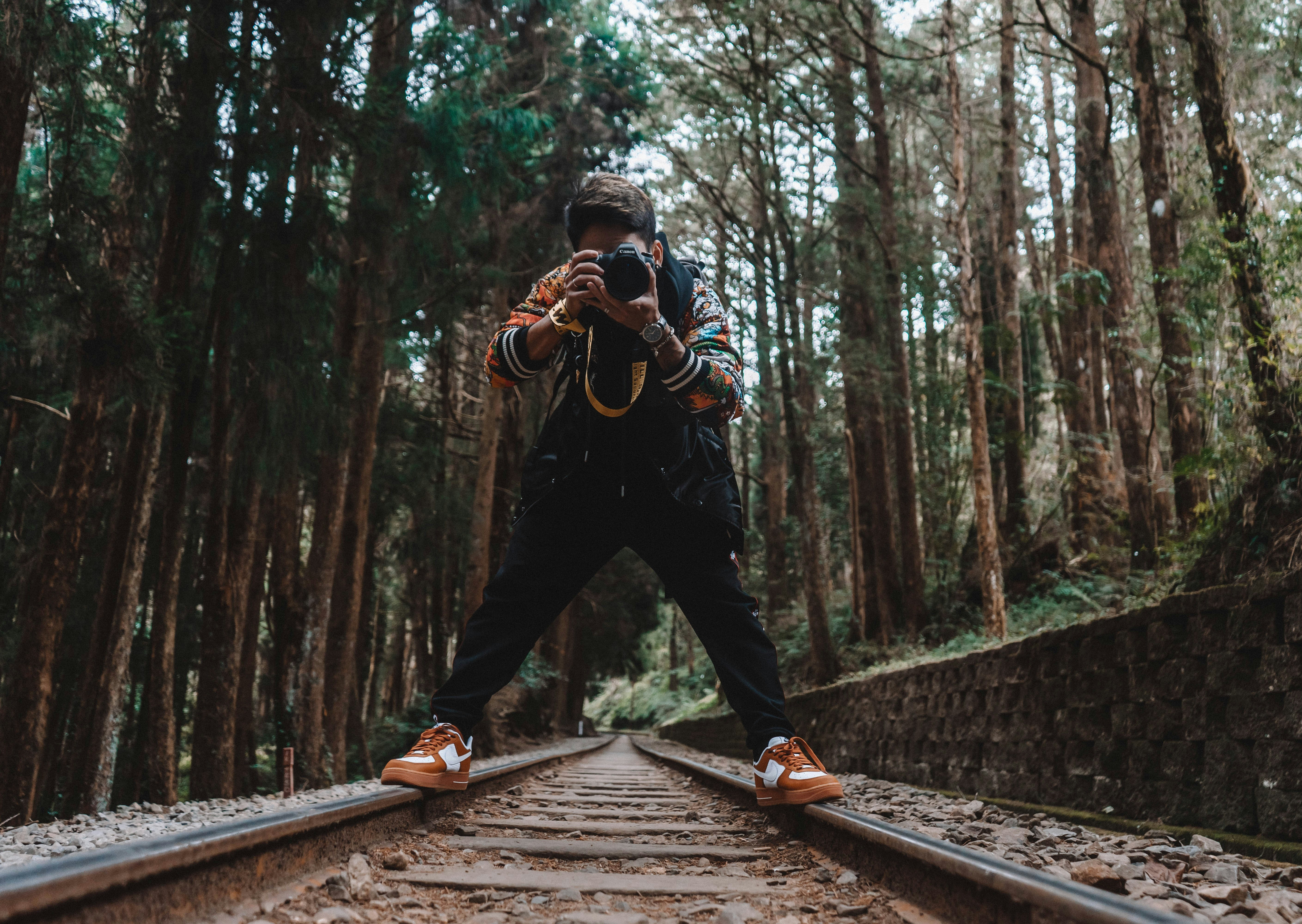 man in black jacket and black pants standing on brown wooden bridge