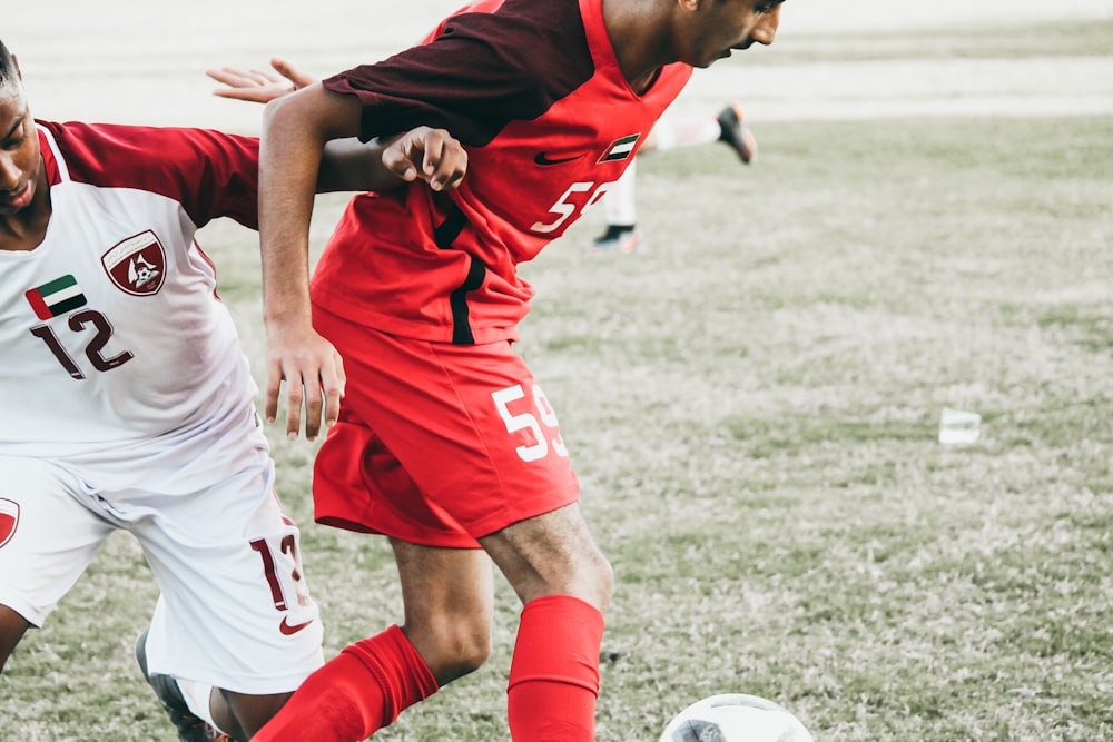 man in red and white soccer jersey kicking soccer ball on green grass field during daytime