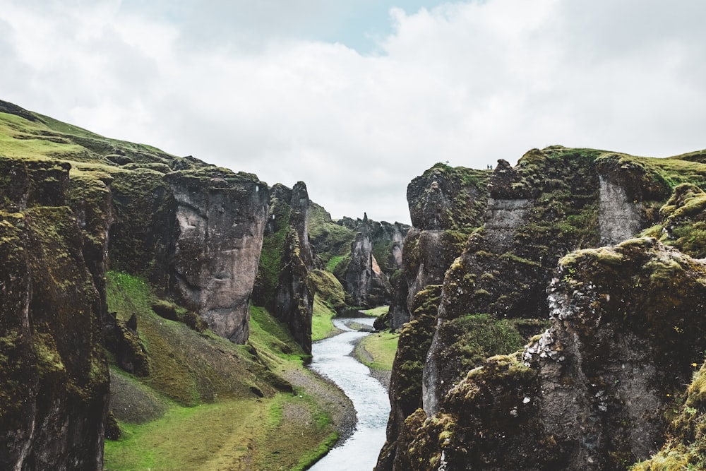 river between green and gray rocky mountain under white cloudy sky during daytime