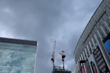 Tall office buildings frame the photo with one building featuring large signs in Japanese. In the background, a crane is visible on a construction site and a small airplane flies in the overcast sky.