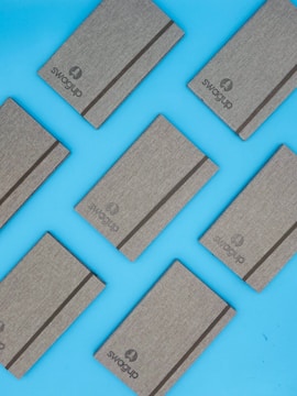 Several gray notebooks with elastic bands are arranged diagonally on a bright blue background. The word 'Swagup' is printed on each notebook.