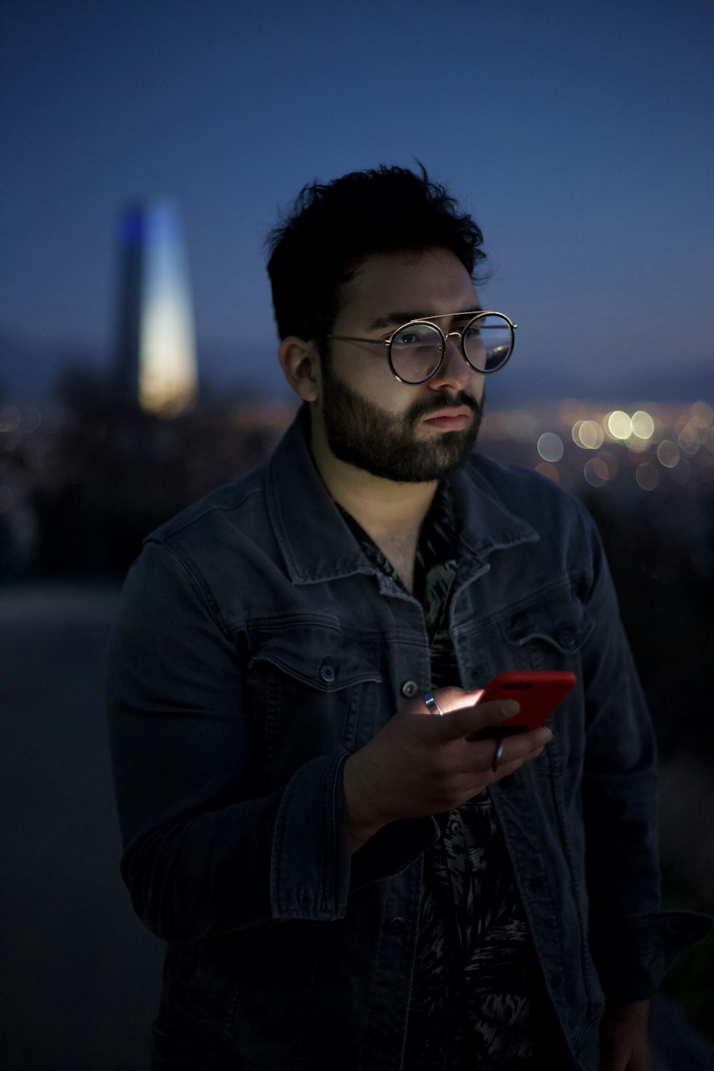 man in black leather jacket holding red smartphone during night time