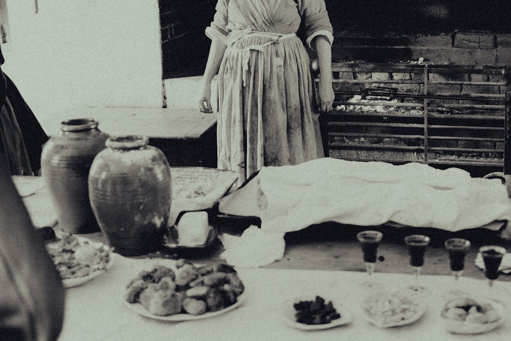 grayscale photo of woman in dress standing in front of cake