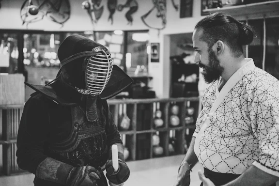 A friendly karate instructor answering questions at a dojo reception desk.