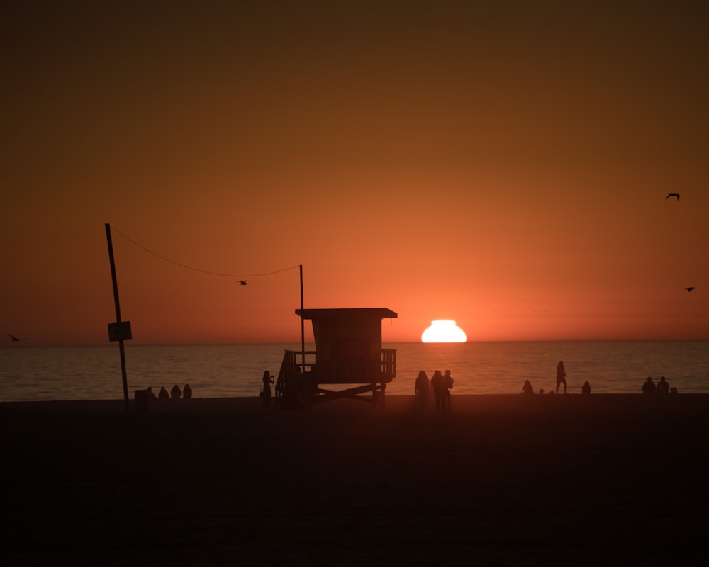 Silueta de la gente en la playa durante la puesta del sol