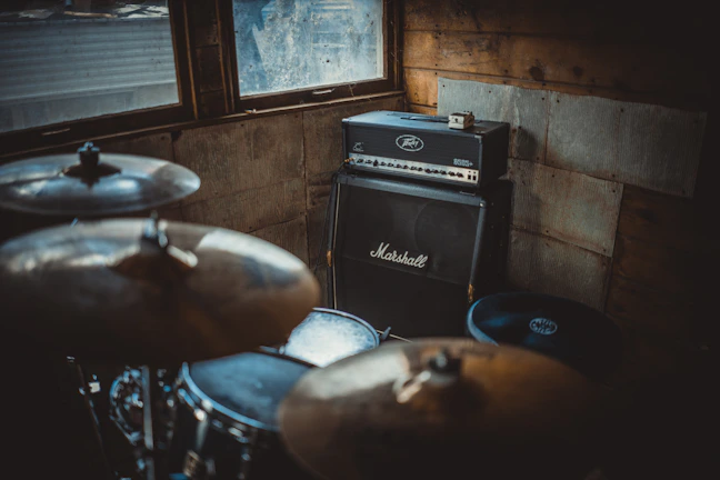 Vintage amplifier and drum set beside a crate of Ritmo Ámbar beers in a gritty rehearsal space.