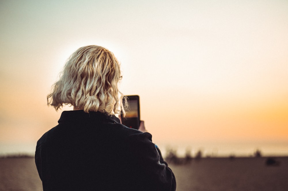 person in black jacket taking photo of sunset