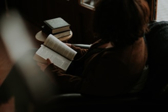 A thoughtful person reading a book in a cozy, well-lit space.