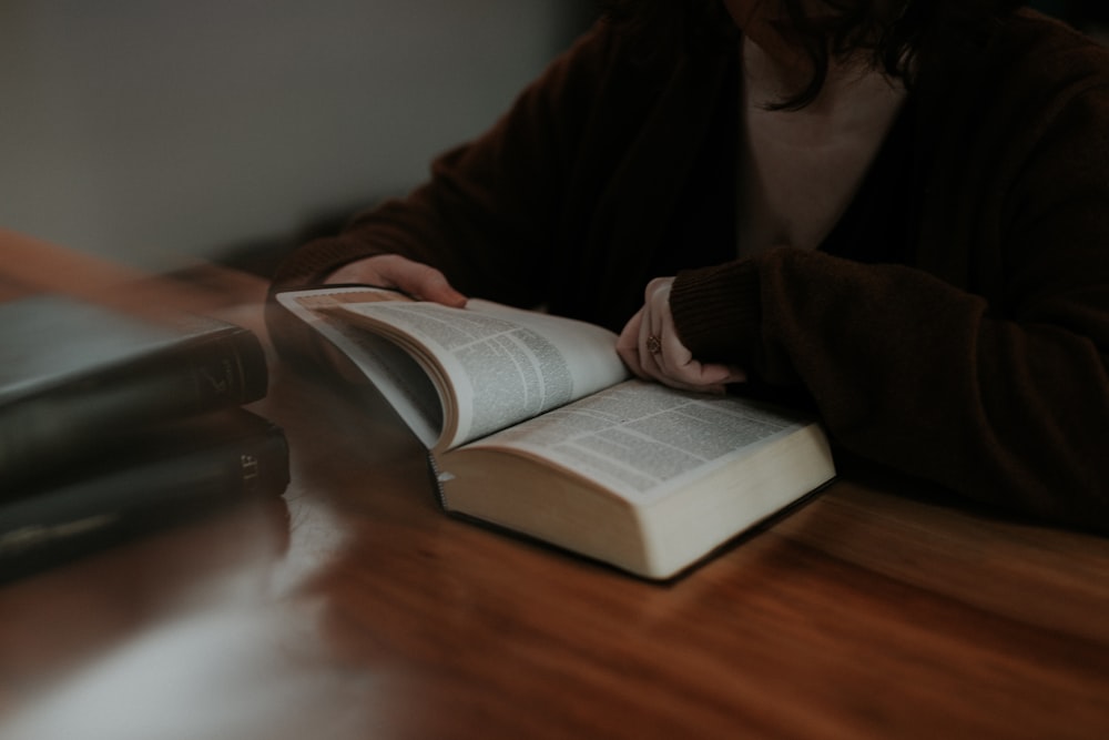 persona leyendo un libro sobre una mesa de madera marrón