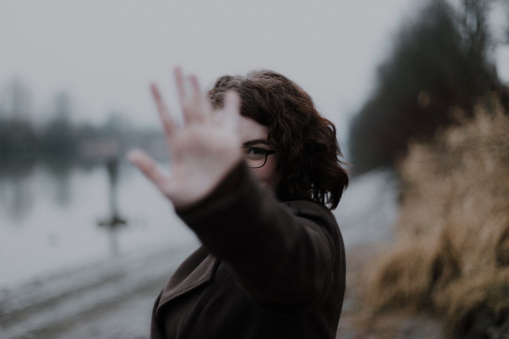 femme en manteau noir debout près d’un plan d’eau pendant la journée